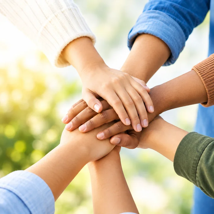 A diverse group stacking hands together in the sunshine